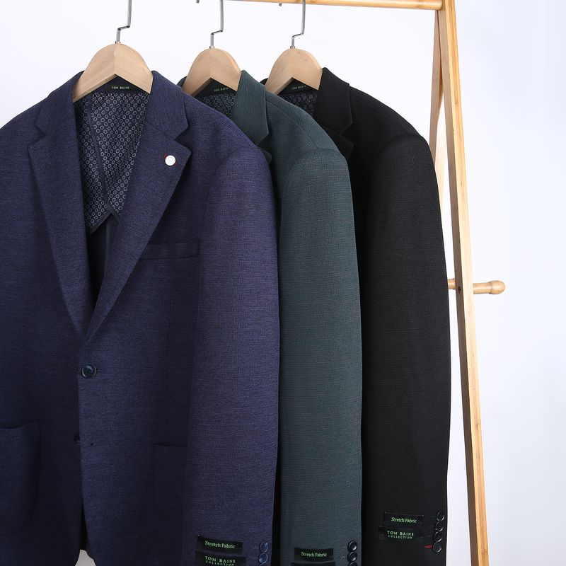 Three Tom Baine stretch fabric sportcoats in navy, green, and black on a wooden rack